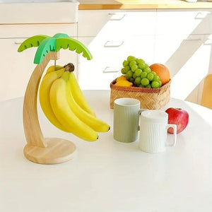 Banana holder shaped like a palm tree with bananas, a basket of fruit, and mugs on a kitchen counter.