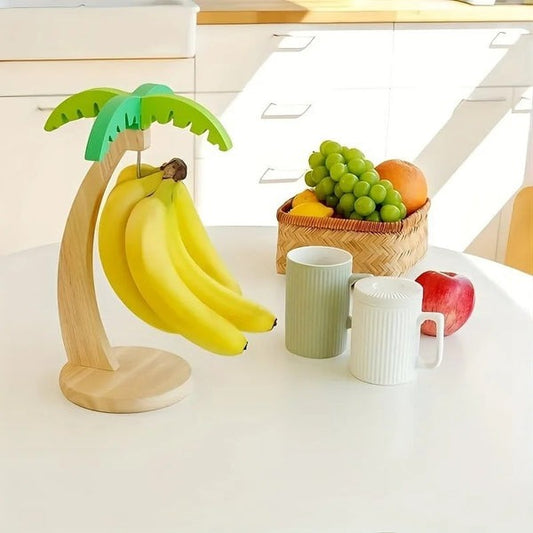 Banana holder shaped like a palm tree with bananas, a basket of fruit, and mugs on a kitchen counter.
